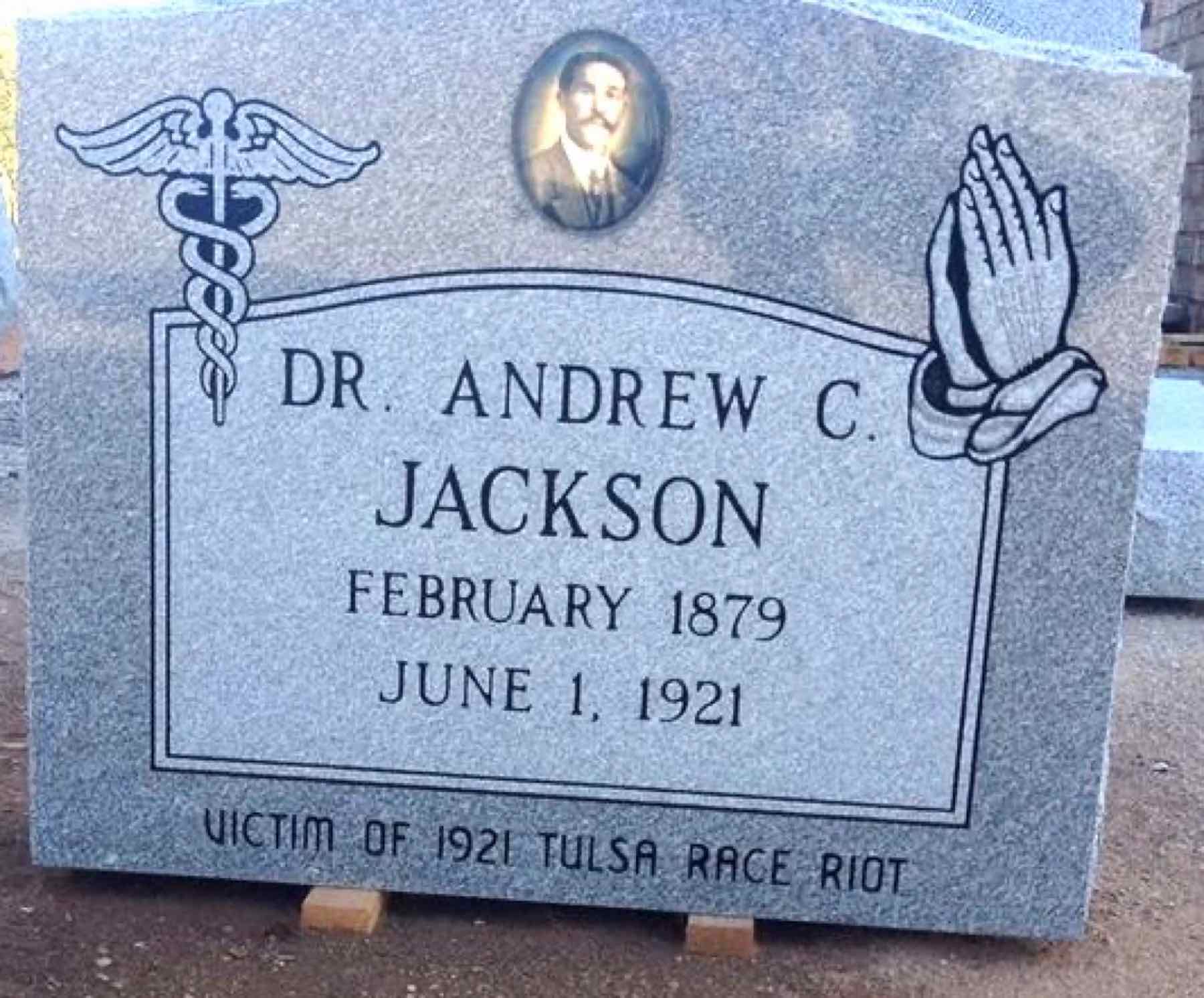 The headstone face: 'DR. ANDREW C. JACKSON · FEBRUARY 1879 · JUNE 1, 1921 · VICTIM OF 1921 TULSA RACE RIOT,' with a caduceus for his medical practice, praying hands, and a ceramic oval portrait — photographed at the monument works before installation